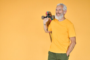 Fototapeta na wymiar Active smiling happy cool gray haired bearded old senior man skater wearing t-shirt holding skateboard standing isolated on yellow background. Older people freedom spirit concept. Copy space