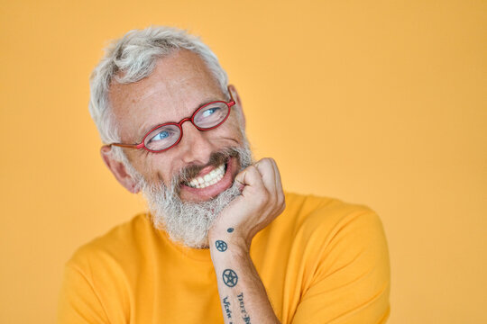 Cunning Excited Older Senior Funny Man Looking Away At Copy Space. Sneaky Old Mature Bearded Hipster Wearing Glasses Waiting With Anticipation Expectation Isolated On Yellow Background.