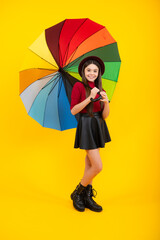 Happy teenager portrait. Teen girl with umbrella in autumn weather isolated on yellow background. Autumn kids clothes.