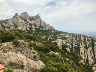 Fototapeta na wymiar Montserrat, Spain, June 2019 - A rocky mountain with trees in the background with Montserrat in the background
