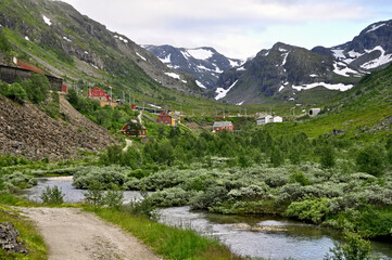 Fototapeta na wymiar Myrdal, Norway - a small village with a few houses and a railway station high in the mountains. River and red houses under snowy mountains.