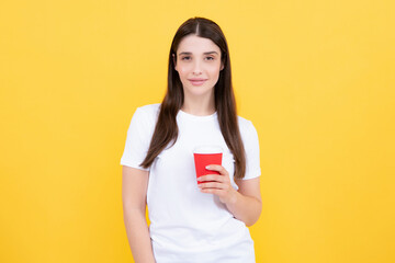 Portrait of a beautiful young woman with a cup of coffee standing on the yellow background.