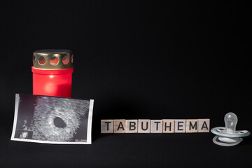 Buchstaben mit dem Wort Tabuthema mit Kerze und Ultraschallfoto auf schwarzen Hintergrund