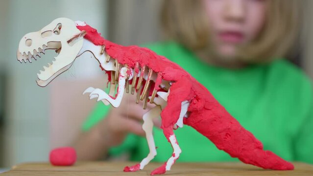 A blonde little girl makes a dinosaur craft out of wood and air plasticine. 