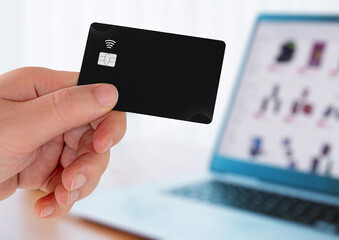 Hand holding a black plastic credit card and using laptop. Online shopping concept