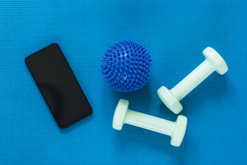 Top view of modern smartphone with black screen on sports mat with ball and dumbbells. Flat lay, mockup. Online training concept