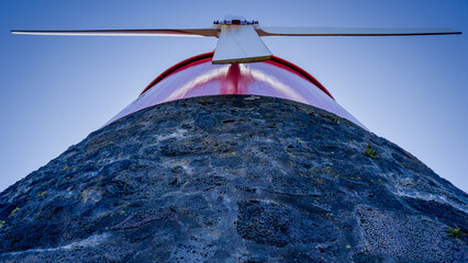 Red mill on a stone base with white blades in the shape of a cross