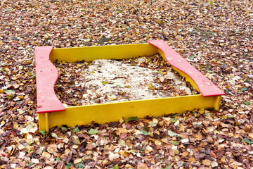 Children's sandbox surrounded by fallen autumn leaves.