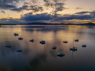 Fototapeta premium Aerial sunrise waterscape with boats, rain clouds and reflections