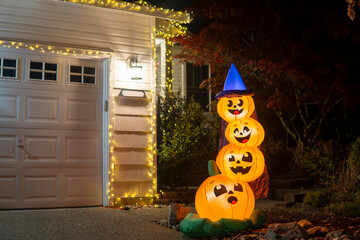 Glowing night Halloween house outdoor decoration with pyramid of witch pumpkins and yellow garlands