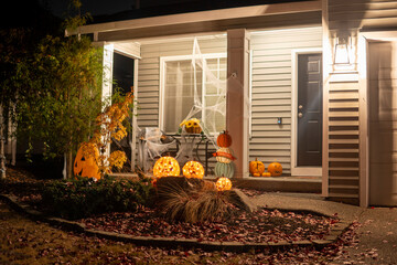 Illuminated night Halloween house outdoor decorations with orange pumpkins and spider web