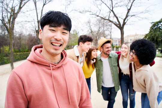 Young smiling asian guy looking at the camera outdoors with group of friends. Happy people having fun together Focus on a young Chinese man. University Colleagues at campus. High quality photo