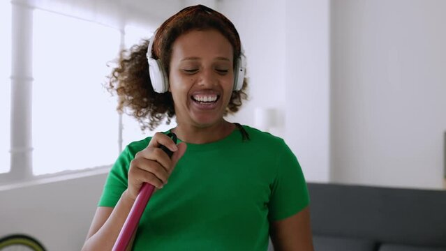 Happy young african american woman having fun singing while cleaning home with broom. High quality 4k footage