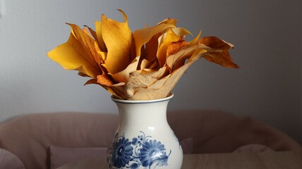 Still life of golden yellow leaves in a white porcelain vase with blue floral patterns.