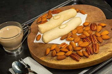 Tuinposter Closeup shot of long almond cookies on a wooden board along with almonds, pecans and a cup of coffee © Luis Alfredo Gonzalez Calkech/Wirestock Creators