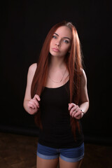 portrait of a beautiful young red-haired girl on a dark black background in the studio, with a cleavage and big breasts in black