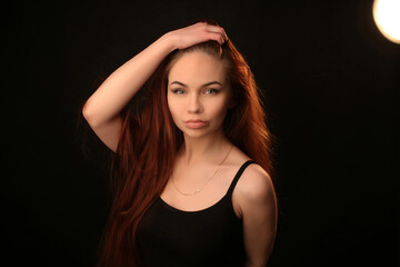 Naklejka premium portrait of a beautiful young red-haired girl on a dark black background in the studio, with a cleavage and big breasts in black