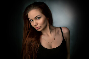 Naklejka premium portrait of a beautiful young red-haired girl on a dark black background in the studio, with a cleavage and big breasts in black
