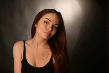 portrait of a beautiful young red-haired girl on a dark black background in the studio, with a cleavage and big breasts in black