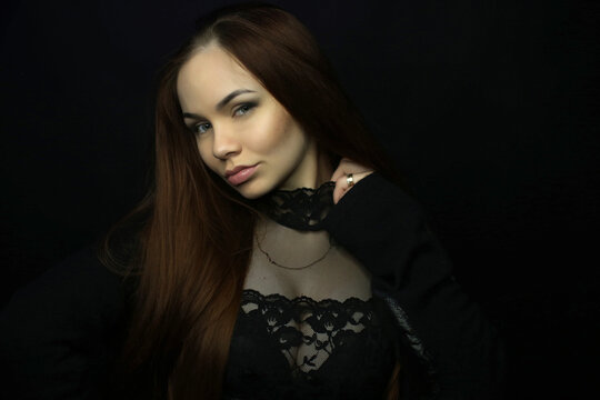 portrait of a beautiful young red-haired girl on a dark black background in the studio, with a cleavage and big breasts in black