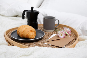 Tray with tasty croissant, cup of coffee and flowers on white bed