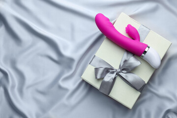 Gift box and pink vaginal vibrator on grey silk fabric, top view with space for text. Sex toy