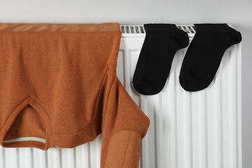 Brown pullover and black socks hanging on white radiator indoors