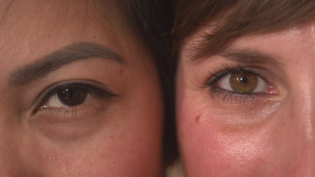 CLOSE UP, PORTRAIT: Detailed view of two young women's brown eyes side by side. Attractive Asian and Caucasian woman looking directly towards camera. Beauty shot of a young ladies' mesmerizing eyes.