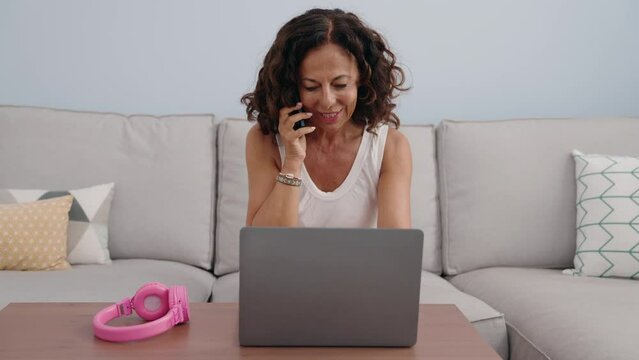 Middle age woman talking on smartphone using laptop at home