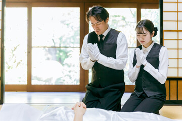 仏衣を着せて合掌する葬儀スタッフ（納棺師）
