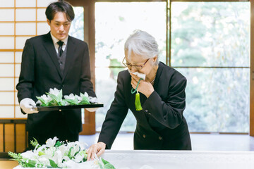お葬式の納棺式で花入れの儀をする高齢者女性（泣く）
