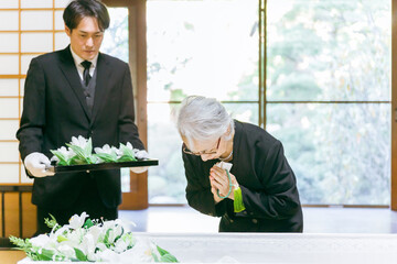 お葬式の納棺式で花入れの儀をする高齢者女性（合掌）
