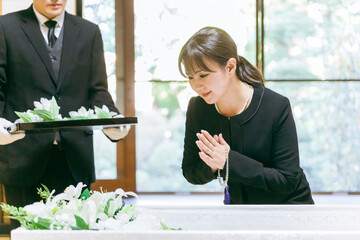 お葬式の納棺で花入れの儀をする日本人女性（笑顔・合掌）
