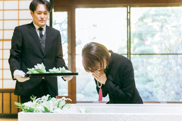 お葬式の納棺で花入れの儀をする日本人女性（合掌）
