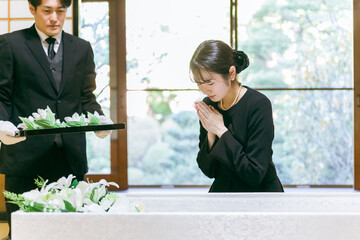 お葬式の納棺で花入れの儀をする日本人女性（合掌）
