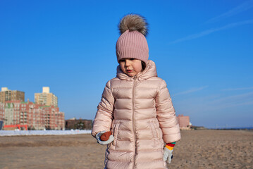 Young girl playing on the beach in winter dressed in a warm coat