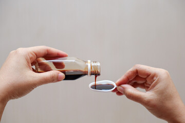 hand pours cough syrup, fever medicine and cold medicine containing paracetamol into a measuring spoon. - obrazy, fototapety, plakaty