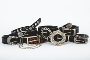 Different types of black leather and animal print belts with variety of buckles on white background