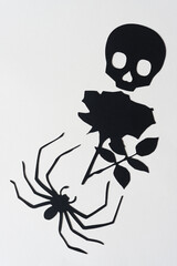 black paper skull, rose, and spider on blank paper