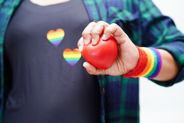 Asian woman holding red hert with rainbow flag, LGBT symbol rights and gender equality, LGBT Pride Month in June.