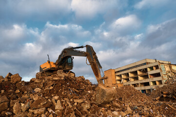 Bucket of excavator digs leftovers of destroyed building