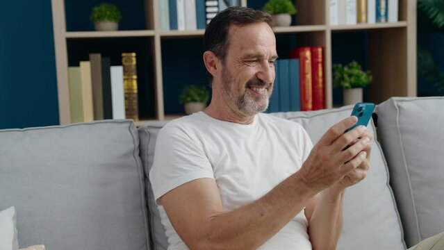 Middle age man using smartphone sitting on sofa at home