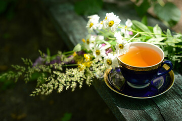 Herbal tea, cup of tea and bouquet chamomile flowers and wildflowers on wooden table in garden,...