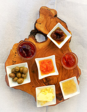 Wood Plank Serving Platter with Seven Small Dishes of Condiments with Jam, Compote, Olives, and Butter