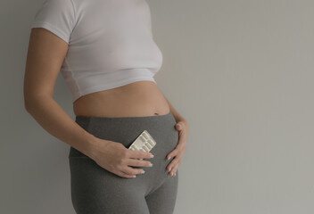 A girl with a belly holds a blister of pills in her hand. Pregnancy. Teenage pregnancy. Problems with the gastrointestinal tract. Soft focus - obrazy, fototapety, plakaty