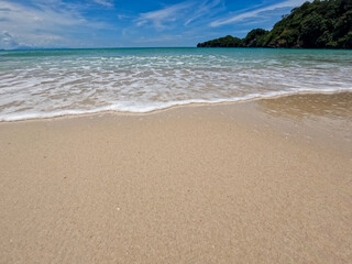 Light blue ocean waves on clean sandy beach. Natural scenery of beautiful tropical beaches and sea on a clear day.