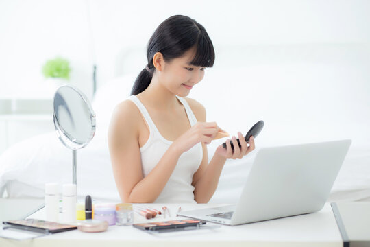 Beauty of young asian woman with learning makeup with powder puff on cheek watching laptop computer with tutorial course online, female teaching and explain make up with cosmetic on streaming media.