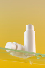 Mockup of white tubes with a cosmetic product on a glass shelf on a yellow background. Skin care