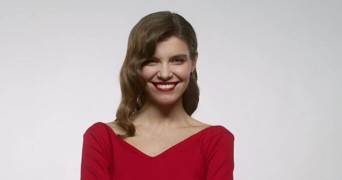 Happy young woman with red lips posing, laughing and sending air kiss, wearing elegant dress, isolated on white studio background