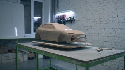 Sculpture of a eco friendly car prototype placed on a wooden table in a workshop with laying sculpting tools. Unfinished sculpture of a prototype model car.